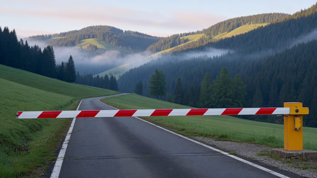 Rot-weiss gestreifte Schranke, die eine ruhige Landstrasse vor Alpenhügeln sperrt